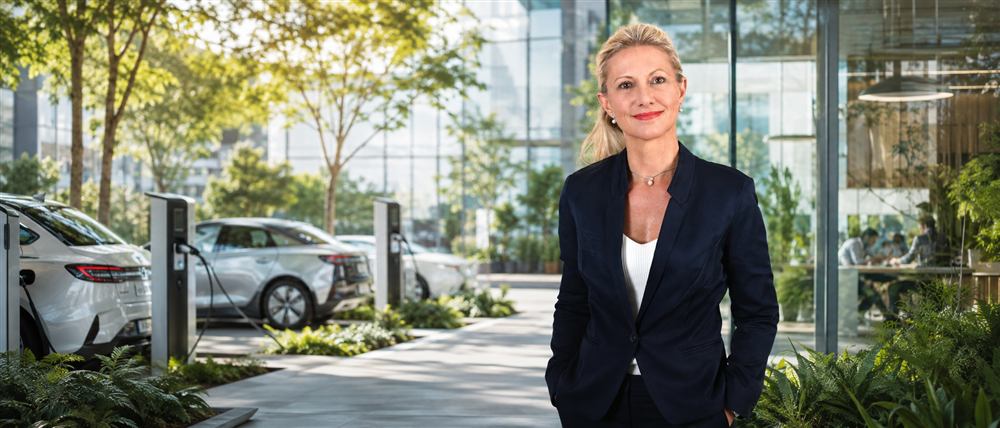 Annette Adler vor Ladesäulen und E-Autos an einem modernen Gebäude